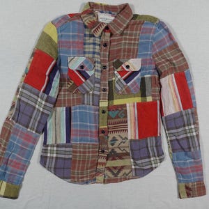 May include: A long-sleeved patchwork shirt with a button-up front and a collar. The shirt is made of different colored plaid fabrics, including blue, red, yellow, and green.