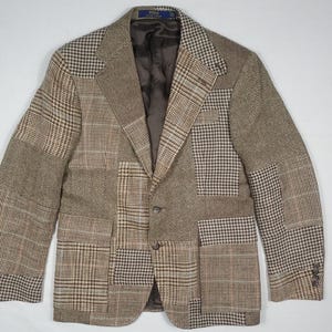 May include: A brown patchwork blazer with various plaid patterns. The jacket features a notched lapel, two buttons, and multiple fabric panels in different shades of brown and tan. The blazer has two front pockets and buttoned cuffs.