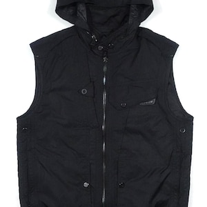 Puede incluir: Chaleco negro con capucha, cremallera completa, dos bolsillos en el pecho y dos bolsillos laterales. El chaleco tiene un dobladillo acanalado y un cuello alto. La capucha está adjunta y tiene un cordón. El chaleco está hecho de un material ligero.