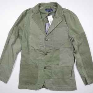 Könnte beinhalten: Olivgrüner Blazer mit Patchwork-Design. Die Jacke hat ein fallendes Revers, einen Drei-Knopf-Verschluss und mehrere Taschen. Ein Etikett ist angebracht. Der Blazer ist ein lässiger Stil.