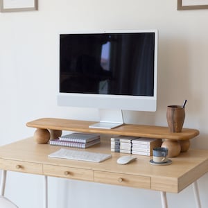 K&ouml;nnte beinhalten: Ein Schreibtisch aus hellem Holz mit einem Computermonitor, Tastatur und Maus. Der Schreibtisch hat drei Schubladen mit runden Holzkn&ouml;pfen. Ein Monitorst&auml;nder aus Holz h&auml;lt B&uuml;cher, eine Tasse und einen Stifthalter. Ein wei&szlig;er Stuhl mit grauem Sitz steht vor dem Schreibtisch.