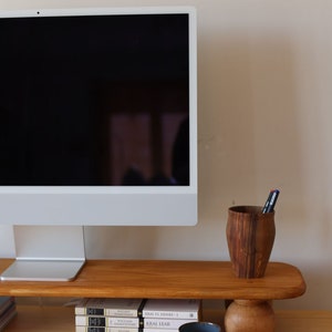 K&ouml;nnte beinhalten: Ein Holzschreibtisch mit einem Computermonitor auf einem Holzst&auml;nder. Eine blau-wei&szlig;e Keramiktasse steht auf einer Untertasse, neben einem Holzstifthalter und einem Stapel B&uuml;cher. Eine Tastatur und eine Maus sind ebenfalls zu sehen.