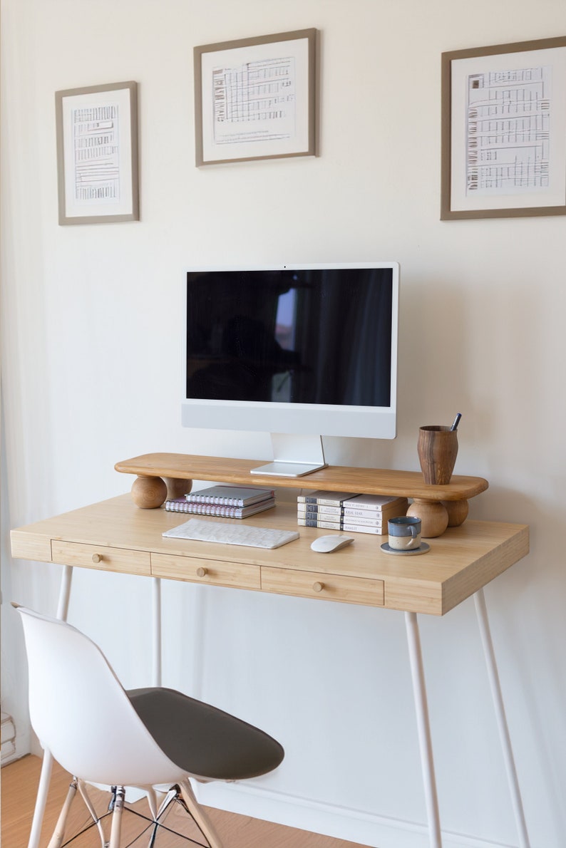 K&ouml;nnte beinhalten: Ein Schreibtisch aus hellem Holz mit einem Computermonitor, Tastatur und Maus. Der Schreibtisch hat drei Schubladen mit runden Holzkn&ouml;pfen. Ein Monitorst&auml;nder aus Holz h&auml;lt B&uuml;cher, eine Tasse und einen Stifthalter. Ein wei&szlig;er Stuhl mit grauem Sitz steht vor dem Schreibtisch.