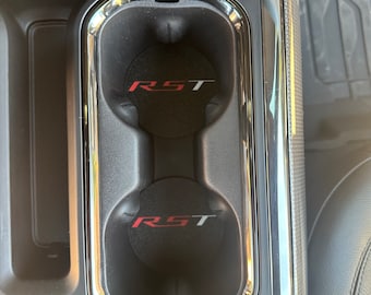 Puede incluir: Dos portavasos negros con ribete cromado. Cada portavasos tiene un posavasos redondo negro con las letras rojas "RST" impresas.