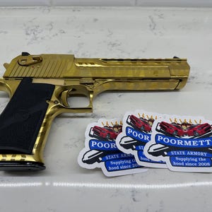 May include: A gold-plated handgun with a black grip and a pattern on the slide. Three stickers are visible in the background, each featuring a red car and the text "POOR" or "POORMETTO" with the words "STATE ARMORY" and "Supplying the hood since 2008".