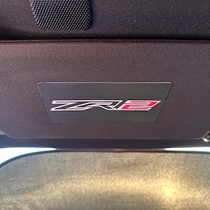 May include: A black car sun visor with a red and white "ZR2" logo.