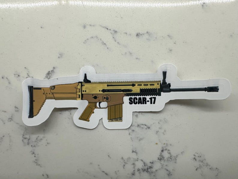 May include: A sticker of a tan and black SCAR-17 rifle with the text "SCAR-17" printed on the sticker.