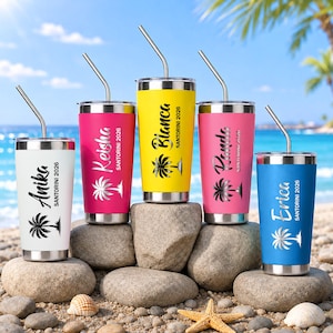 May include: Five stainless steel tumblers with lids and bent metal straws, each featuring a unique name, the text SANTORINI 2026, and a palm tree graphic. The tumblers are white, magenta, yellow, pink, and blue, arranged on a rocky beach surface.
