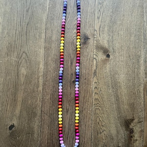 May include: A colorful beaded lanyard with a rainbow gradient of colors, including purple, blue, pink, red, orange, and yellow. The lanyard has silver metal clasps at the top.