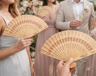 Peut inclure: Éventails en bois avec des motifs découpés complexes. Les éventails sont brun clair avec des motifs décoratifs et du texte. Les éventails sont tenus par des personnes lors d'un mariage. Le texte sur l'éventail indique "Demo & Dom 05.14.16".
