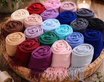 Peut inclure: Une collection de nombreuses écharpes douces roulées en cylindres serrés et disposées dans un grand panier tressé rond. Les écharpes présentent une grande variété de couleurs unies, notamment des tons rouge, rose, violet, bleu, vert, beige, marron et gris.