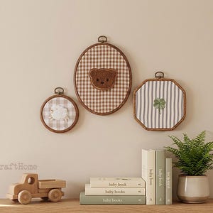 May include: Three embroidery hoops featuring fabric backgrounds and centered motifs: a small circular hoop with a white sheep, a large oval hoop with a brown teddy bear face, and an octagonal hoop with a green four-leaf clover embroidery.