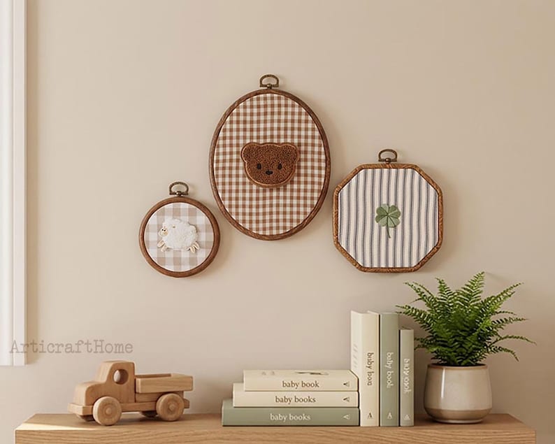 May include: Three embroidery hoops featuring fabric backgrounds and centered motifs: a small circular hoop with a white sheep, a large oval hoop with a brown teddy bear face, and an octagonal hoop with a green four-leaf clover embroidery.