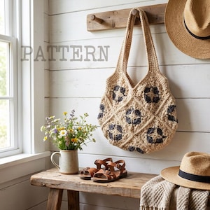 Puede incluir: Un bolso tote de crochet beige con detalles florales azul oscuro cuelga de una clavija de madera. La palabra "PATTERN" está impresa en la pared. Un sombrero de paja, sandalias y un jarrón con flores están en un banco de madera.