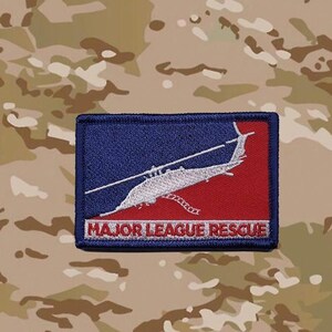 May include: A rectangular embroidered patch with a dark blue border. The design features a white helicopter silhouette over a split blue and red background, with the text MAJOR LEAGUE RESCUE printed in red letters at the bottom.