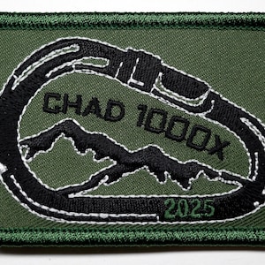 Könnte beinhalten: Gestickter Aufnäher mit grünem Hintergrund und schwarzem Karabiner-Design. Der Text "CHAD 1000X" und "2025" sind in Weiß und Grün gestickt. Der Aufnäher hat einen grünen Rand.