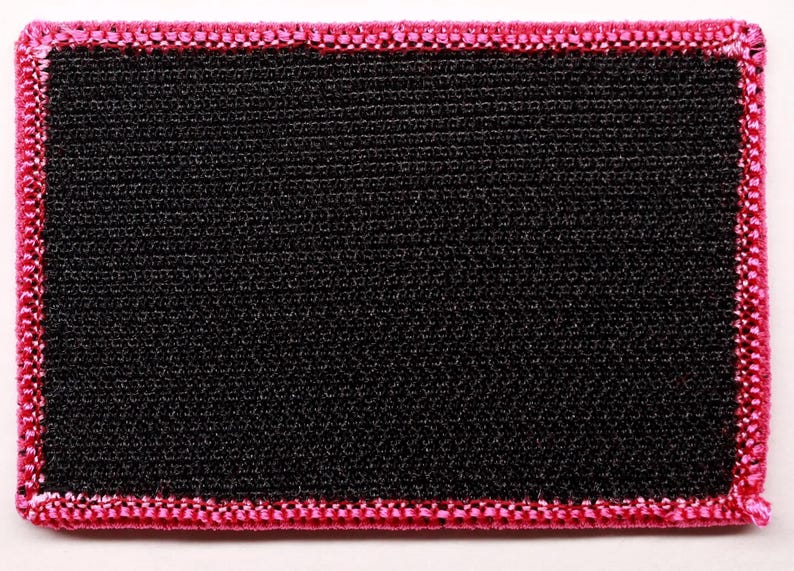 May include: A rectangular patch featuring a solid black center with a textured, woven fabric surface. The edges of the patch are finished with a thick, vibrant pink embroidered border that frames the black rectangular center completely.
