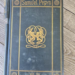 May include: A dark blue hardback book with gold lettering and decorative accents. The title is "Samuel Pepys and the World He Lived In".