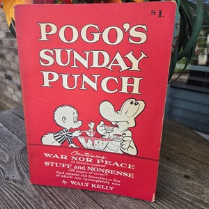 Könnte beinhalten: Ein rotes Buch mit dem Titel "POGO'S SUNDAY PUNCH" und einem Preisschild von 1 $. Der Umschlag zeigt eine Comic-Illustration von zwei Figuren, eine mit einem gestreiften Hemd und die andere mit einem weißen Hemd, die an einem Tisch mit Schüsseln voller Essen sitzen. Der Text auf dem Umschlag lautet "Containing WAR NOR PEACE (A Novel treatment) STUFF and NONSENSE (28 pages of verse?) And several old favorites, a few of which are incompletely new by WALT KELLY."