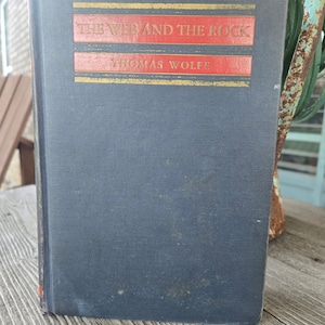 May include: A dark blue hardback book with gold lettering on the spine and front cover. The title of the book is "The Web and the Rock" by Thomas Wolfe.