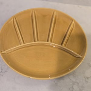 May include: A light brown ceramic serving dish with five divided sections. The dish is round and has a slightly raised rim.