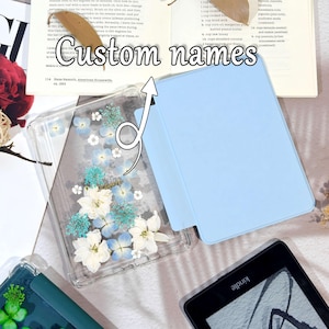 K&ouml;nnte beinhalten: Eine transparente Handyh&uuml;lle mit gepressten wei&szlig;en und blauen Blumen und dem Wort "Love". Daneben befindet sich eine hellblaue Tableth&uuml;lle. Der Text "Custom names" ist im Bild. Ein Kindle-E-Reader ist ebenfalls sichtbar.