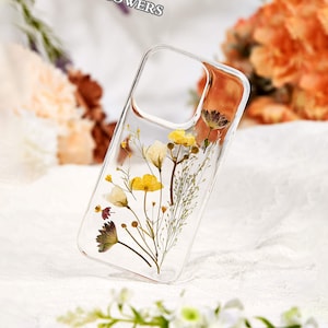 Peut inclure: Une coque de téléphone transparente avec des fleurs pressées à l'intérieur. Les fleurs sont jaunes, blanches et brunes. La coque est conçue pour s'adapter à un smartphone.