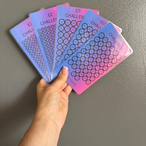 May include: A set of six colourful cards with a gradient background. Each card has a different amount of money printed on it, ranging from £1 to £20. The cards are labelled "Challenge" and have a grid of circles with numbers printed on them. The total value of the cards is £1000.