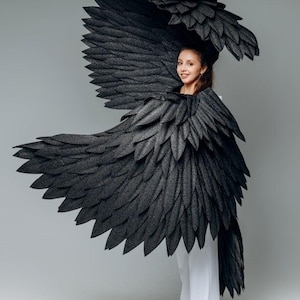 May include: A woman wearing a white outfit with large black feathered wings. The wings are made of many individual feathers and are very detailed.