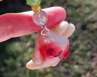 May include: A small white and red bunny charm with blue eyes, hanging from a silver chain with colorful beads.