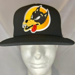 May include: Black trucker hat with a yellow, white, and red cartoon wolf graphic. The wolf has a tongue sticking out and is wearing a white collar.