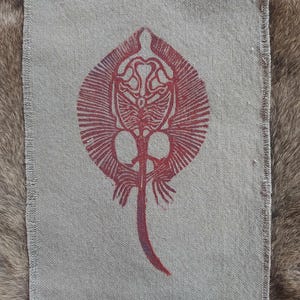 Peut inclure: Un motif imprimé rouge et blanc d'une raie sur un fond de tissu beige. Le motif est détaillé et complexe, avec le corps et la queue de la raie clairement visibles.