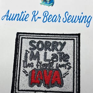 Puede incluir: Parche bordado con el texto "SORRY I'M LATE the floor is LAVA" en negro y rojo. El parche tiene un fondo blanco con un borde negro. La imagen también incluye el texto "Auntie K-Bear Sewing" y un oso de dibujos animados.