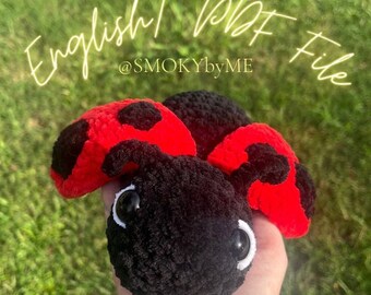 May include: A black and red crocheted ladybug plush toy. The ladybug has large, white eyes and a black body with red spots. The text "English | PDF File @SMOKYbyME" is visible in the image.