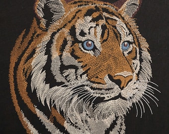 Pode incluir: Close-up do rosto de um tigre com olhos azuis. O tigre é bordado em um fundo de tecido preto.