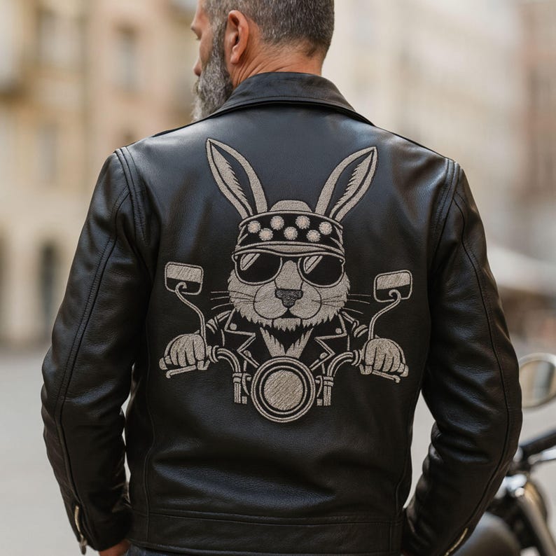 May include: Black leather jacket featuring a biker bunny graphic on the back. The bunny is wearing sunglasses and a bandana, riding a motorcycle. The jacket has a classic biker style with a notched collar and zipper details.