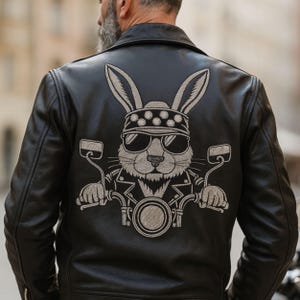 Könnte beinhalten: Schwarze Lederjacke mit einem gestickten Design eines Hasen mit Sonnenbrille und Bandana, der Motorrad fährt. Die Jacke hat einen klassischen Biker-Stil mit Reverskragen und Reißverschlusstaschen.