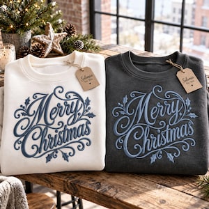 May include: Two crewneck sweatshirts, one cream and one charcoal gray, each featuring blue embroidered text that reads Merry Christmas with decorative swirls and holly leaves. A brown paper tag labeled Solomia for You is attached to each collar.