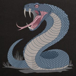 Könnte beinhalten: Eine gestickte Schlange in Blau und Grau mit einer rosa Zunge und roten Augen. Die Schlange ist in einer defensiven Position zusammengerollt, mit erhobenem Kopf und offenem Maul.