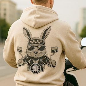 May include: Beige hoodie with a graphic of a rabbit wearing sunglasses, a bandana, and a leather jacket, riding a motorcycle. The design is in black and gray. The hoodie has a hood and long sleeves.