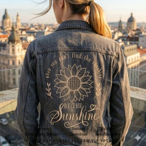 Puede incluir: Chaqueta vaquera gris oscuro con un diseño de girasol bordado en la espalda. El diseño incluye el texto "when you can't find the sunshine, be the sunshine". La chaqueta es de estilo clásico con botones.