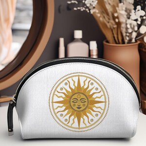 May include: White cosmetic bag with a gold sun design. The sun has a smiling face and is surrounded by a gold circle with dots. The bag has a black zipper and a black handle.