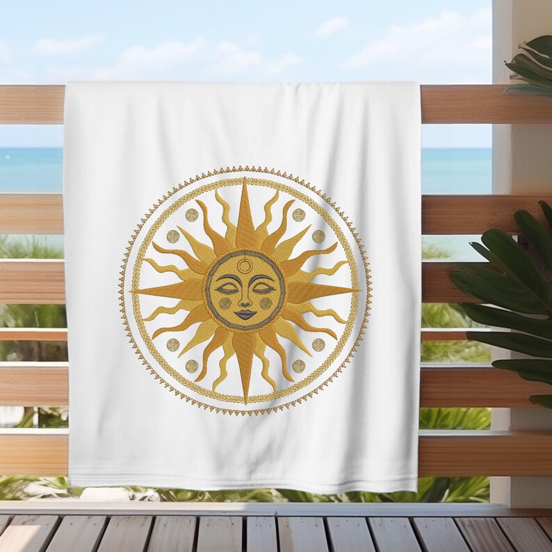 May include: White beach towel featuring a detailed sun design with a smiling face, radiating golden rays, and a decorative border. The sun design is centered on the towel, which is hanging on a wooden railing with a view of the ocean.