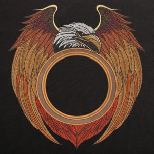 Könnte beinhalten: Ein gesticktes Design mit einem Adler mit ausgebreiteten Flügeln, einem runden Rahmen und einem schwarzen Hintergrund. Der Kopf des Adlers ist zum Betrachter gewandt, und die Flügel sind symmetrisch ausgebreitet. Der Rahmen ist aus goldfarbenem Material gefertigt und hat eine glatte, polierte Oberfläche.