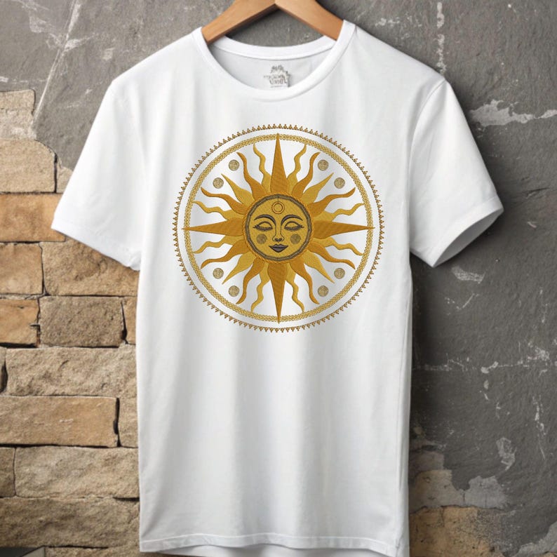 May include: White t-shirt featuring a golden sun design with a smiling face and radiating beams. The sun is encircled by a decorative border. The shirt is displayed on a wooden hanger against a textured wall.
