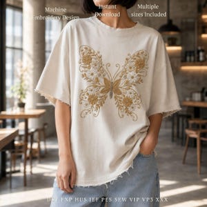 May include: Cream-colored t-shirt featuring a detailed butterfly embroidery design in shades of gold and white. The shirt has a relaxed fit with raw edges on the sleeves. Text on the shirt includes "Machine Embroidery Design" and "Instant Download."