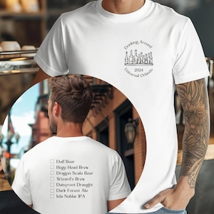 Puede incluir: Camiseta blanca con una lista de cervezas en la espalda y un gráfico de botellas de cerveza con el texto "Drinking Around 2024 Universal Orlando" en el frente.