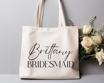 May include: A white canvas tote bag with black handles and the text "Brittany Bridesmaid" printed on the front.