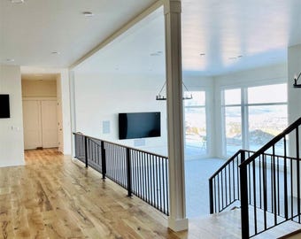 May include: A hallway with hardwood floors and a black metal railing leading to a lower level. The hallway has white walls and a white ceiling with recessed lighting.