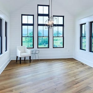May include: A white room with a wooden beam ceiling and large black windows. The room has a white chair and a small table in the corner. The floor is made of light brown wood.